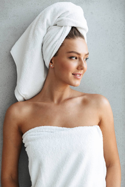 Beautiful young woman wrapped in a bath towel standing at the wall at home - Photo, image
