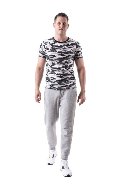 Happy smiling fit man in sport sweatpants and army shirt walking and looking at camera. Full body isolated on white background.  - Foto, afbeelding