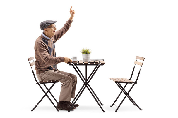 Full length profile of an elderly man sitting at a coffee table and calling a waiter isolated on white background - Фото, изображение