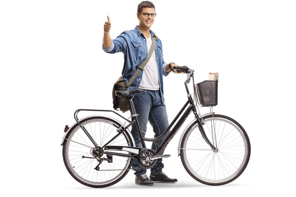 Full length shot of a young smiling man standing with a bicycle and giving thumbs up isolated on white background - Zdjęcie, obraz