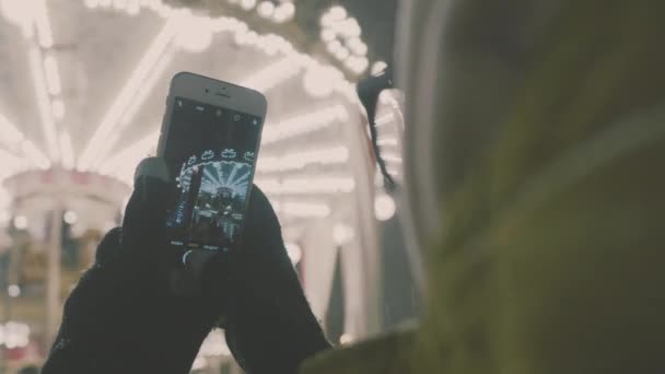 Γυναίκα λήψη φωτογραφιών της Ευρωπαϊκής carousel σκηνή στο Smartphone. 4 k. κορίτσι απολαμβάνει χειμερινές διακοπές σεζόν - Πλάνα, βίντεο