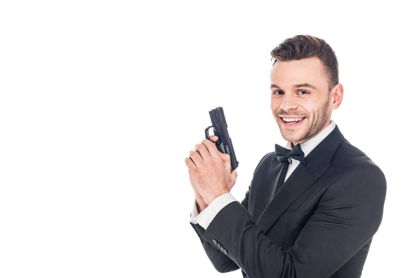 cheerful secret agent in black suit holding gun, isolated on white - Fotó, kép
