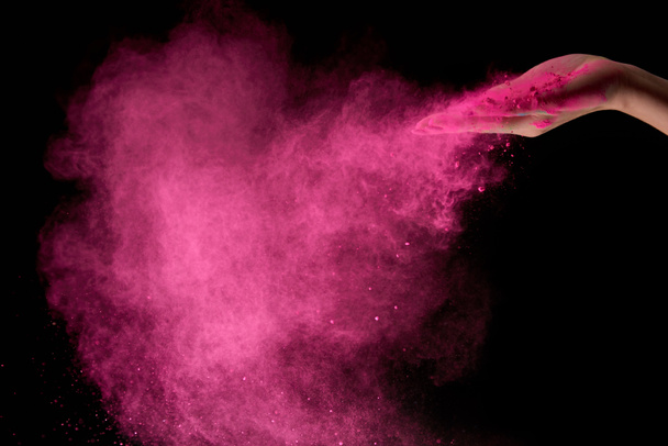 vista recortada de la mujer adulta con polvo de holi rosa en el aire sobre fondo negro
 - Foto, Imagen