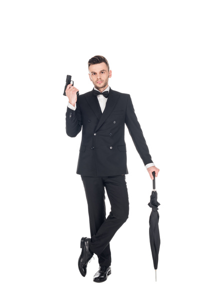handsome killer in tuxedo holding handgun and umbrella, isolated on white - Photo, Image