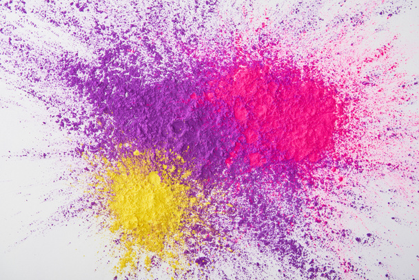 top view of explosion of purple, pink and yellow holi powder on white background - Fotografie, Obrázek