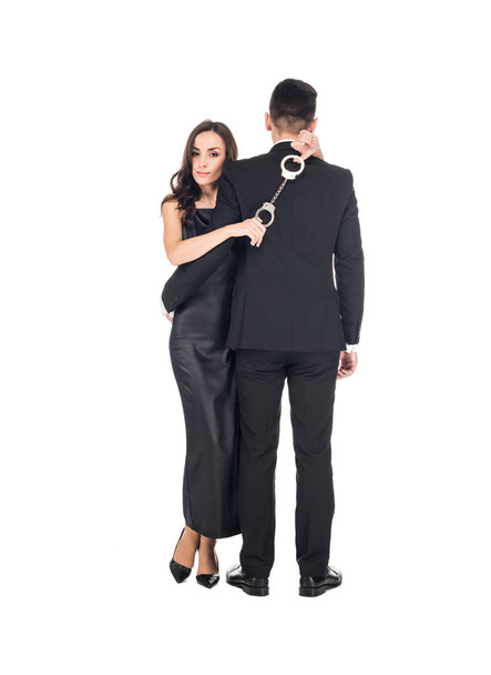 elegant woman in black dress hugging man and holding handcuffs, isolated on white - Φωτογραφία, εικόνα