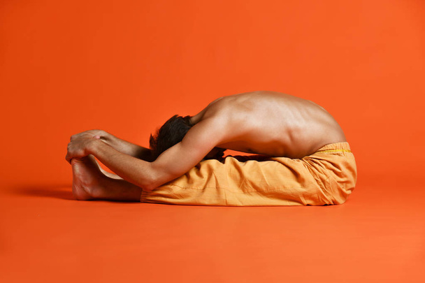 old man practices Ashtanga Vinyasa yoga back bending asana Paschimottanasana - seated forward bend - Fotó, kép