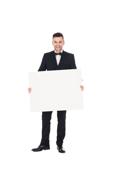 handsome smiling elegant man in black suit posing with empty board isolated on white - 写真・画像