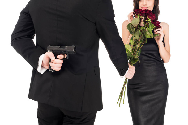 vista trasera del hombre regalando rosas rojas mientras oculta el arma detrás de la espalda, aislado en blanco
 - Foto, Imagen