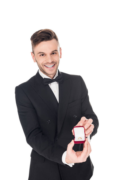 happy man in black tuxedo holding proposal ring in box, isolated on white - Фото, изображение