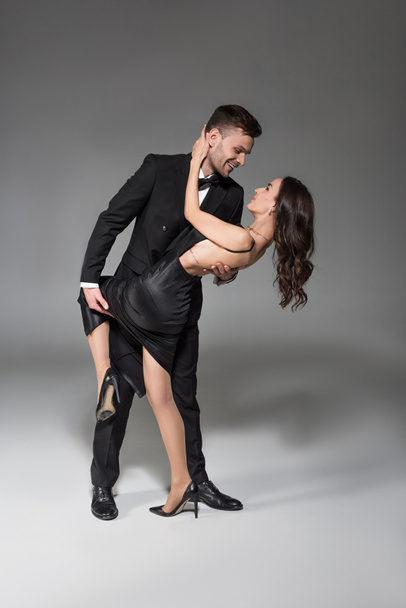 beautiful elegant couple in black clothes hugging and dancing on grey - Photo, Image