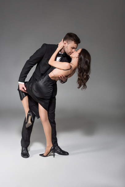 young handsome man kissing beautiful elegant girlfriend on grey  - Фото, зображення