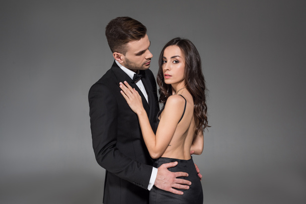 attraktives elegantes Paar in schwarzer Kleidung, das sich isoliert auf grau umarmt - Foto, Bild
