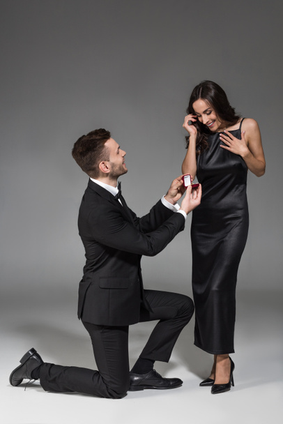 young boyfriend holding proposal ring in box for attractive girlfriend on grey - Φωτογραφία, εικόνα