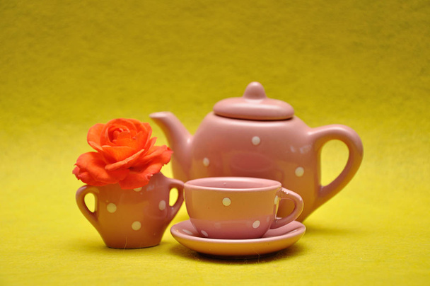 Una taza de té y una tetera con una rosa naranja sobre un fondo amarillo
 - Foto, Imagen