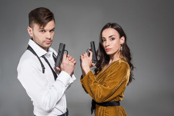 élégant couple confiant d'agents secrets posant avec des armes de poing, isolé sur gris
 - Photo, image