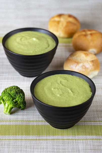 broccoli cream soup in a plate on a dark wooden background. next to a bowl of soup are fresh buns. top vie - Fotó, kép
