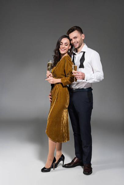 smiling couple hugging and holding champagne glasses on grey - Foto, imagen