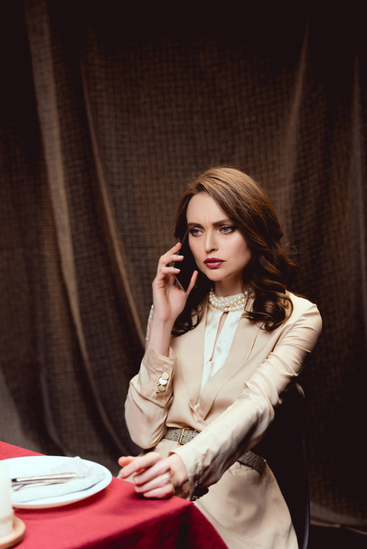 красивая серьезная женщина сидит за столом и разговаривает на смартфоне в ресторане
 - Фото, изображение