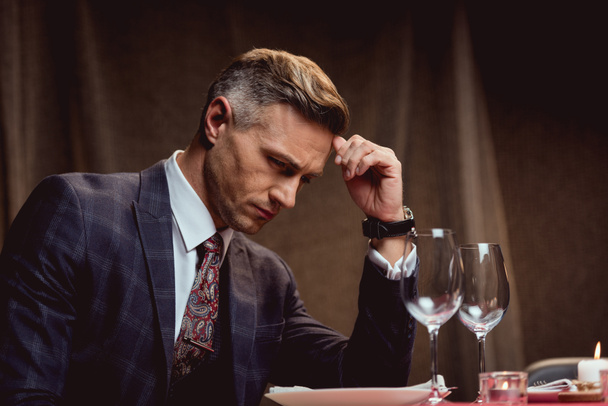 handsome pensive man sitting at table and waiting for someone in restaurant - Foto, Bild