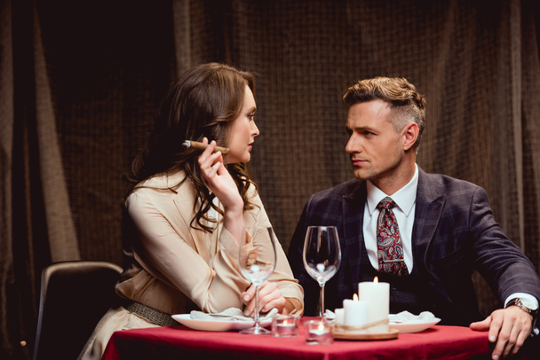 Frau sitzt am Tisch und raucht Zigarre, während sie ein romantisches Abendessen mit einem schönen Mann im Restaurant einnimmt - Foto, Bild