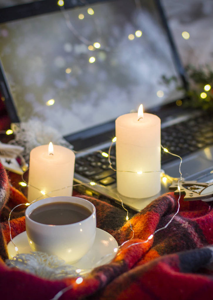 Composición: un portátil, una taza de café (té), velas, guirnaldas y una manta roja
. - Foto, imagen