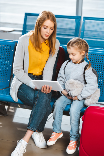  μητέρα της βλέπουν ψηφιακή δισκίο και κάθεται στο αεροδρόμιο με την κόρη  - Φωτογραφία, εικόνα