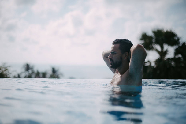 Portret van een jonge knappe man in een buitenzwembad. Aantrekkelijke man met een baard aan de zijkant van het zwembad - Foto, afbeelding