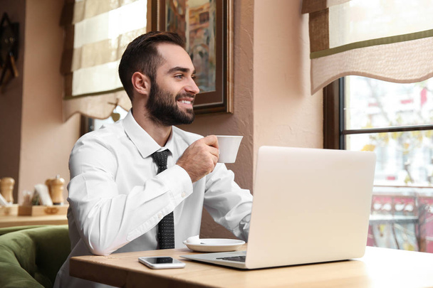 Jeune homme d'affaires buvant du café tout en travaillant sur ordinateur portable dans un café
 - Photo, image