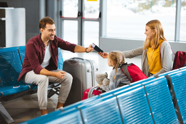 feliz esposa sentada con su hija y dando pasaportes con billetes de avión al marido en el aeropuerto
  - Foto, imagen