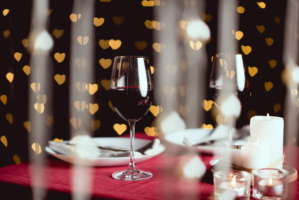 selective focus of red wine glasses with heart shaped bokeh on background - Foto, Imagen
