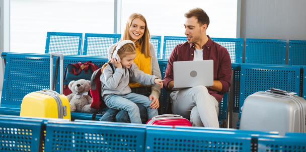 cute daughter pointing with finger at laptop while sitting near dad and mom in airport  - Foto, Imagen