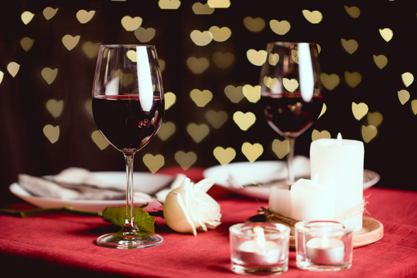 selective focus of red wine glasses with heart shaped bokeh and table setting on background - Foto, Bild