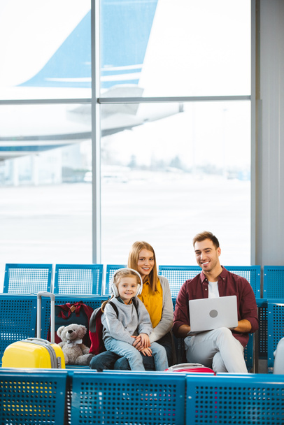 cheerful family smiling while looking at camera in departure lounge - Photo, Image
