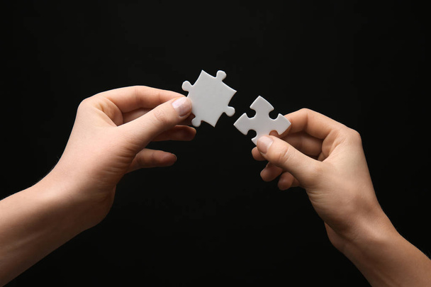 Frauenhände mit Puzzleteilen auf dunklem Hintergrund - Foto, Bild