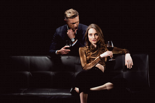 handsome man looking at beautiful woman with glass of red wine isolated on black - Fotoğraf, Görsel