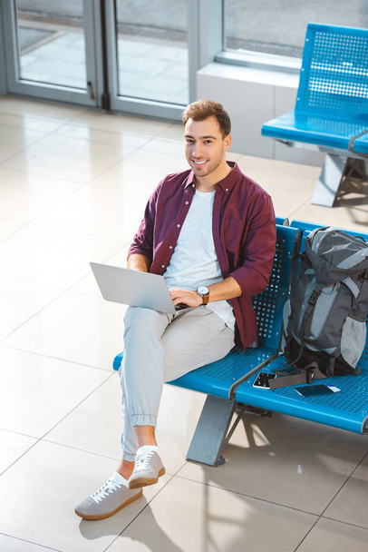 Blick über den Kopf eines lächelnden Mannes mit Laptop, während er in der Abflughalle wartet - Foto, Bild