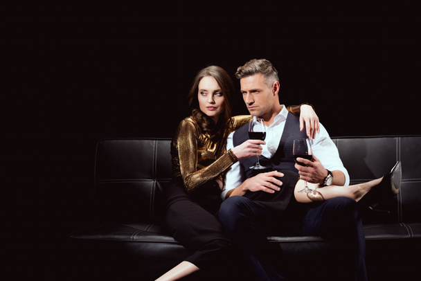 beautiful couple sitting on couch with glasses of red wine isolated on black - Valokuva, kuva