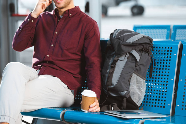 cropped view of man holding paper cup near backpack and laptop  - Photo, Image