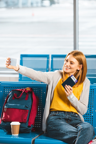 attractive woman taking selfie with passport and air ticket in waiting hall - Foto, Imagem