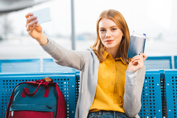 beautiful woman taking selfie with passport and air ticket in waiting hall  - Photo, image
