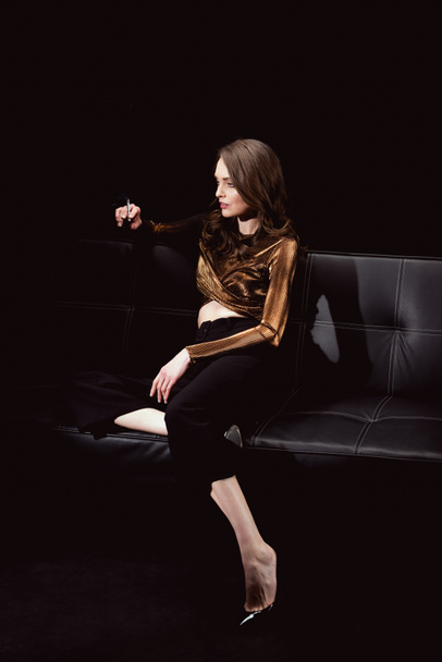 beautiful glamorous woman sitting on couch and smoking cigarette isolated on black - Foto, Imagen