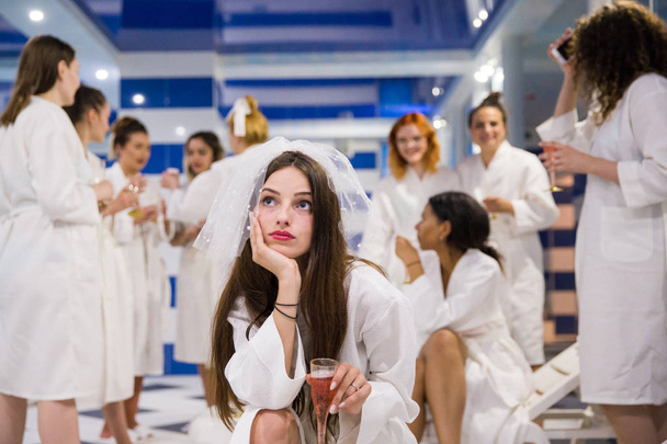 The attractive bride sitting near her friends at the hen party near a pool and holding a glass of champagne - Fotografie, Obrázek