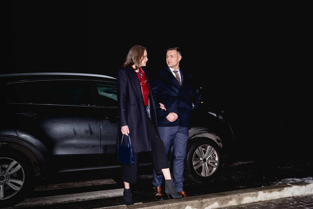 Paar hält Händchen und schaut sich mit Auto im Hintergrund an - Foto, Bild