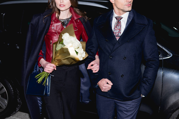cropped view of woman with flower bouquet holding hands with man  - Фото, зображення