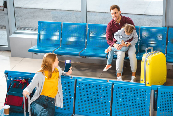 handsome father sitting with daughter in airport near woman with luggage  - Foto, Imagen