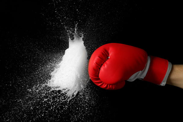 Hand in boxing glove with splashes of liquid on dark background - Photo, Image