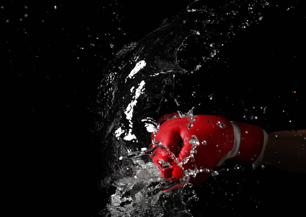 Hand in boxing glove with splashes of liquid on dark background - Foto, afbeelding
