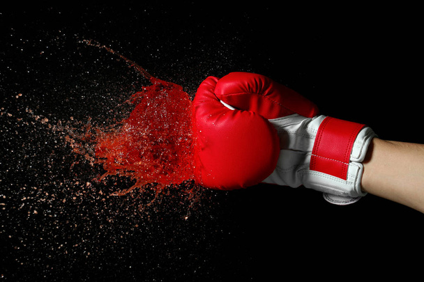 Hand in boxing glove with splashes of liquid on dark background - Photo, Image