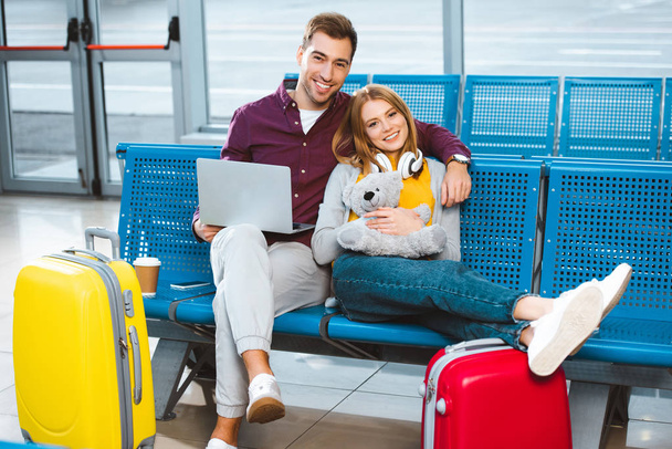 petit ami heureux avec ordinateur portable souriant avec petite amie tenant ours en peluche à l'aéroport
 - Photo, image